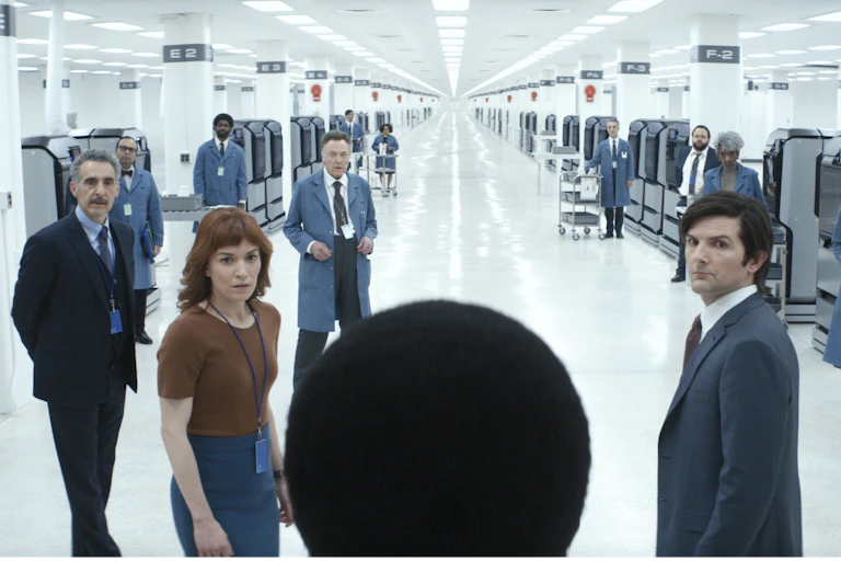 In a white office space, many employees look at a central figure.