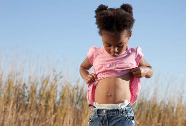 young girl lifts her shirt and looks down at her belly