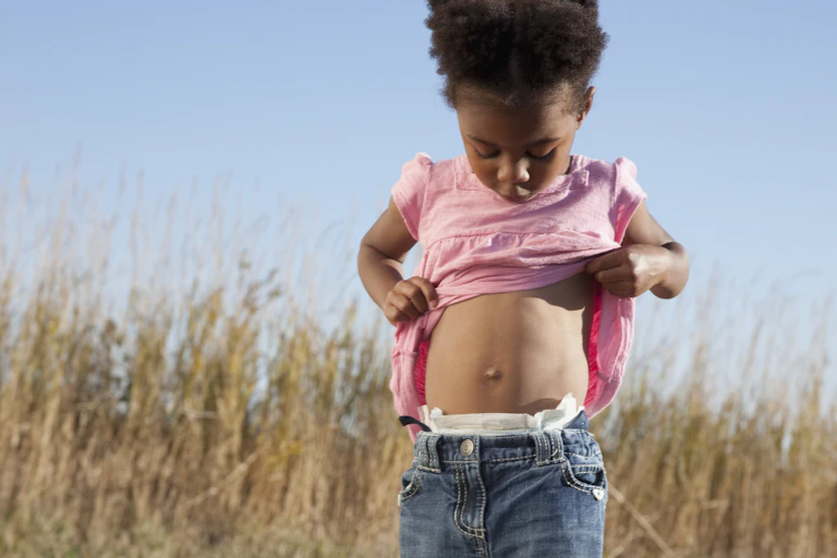 young girl lifts her shirt and looks down at her belly