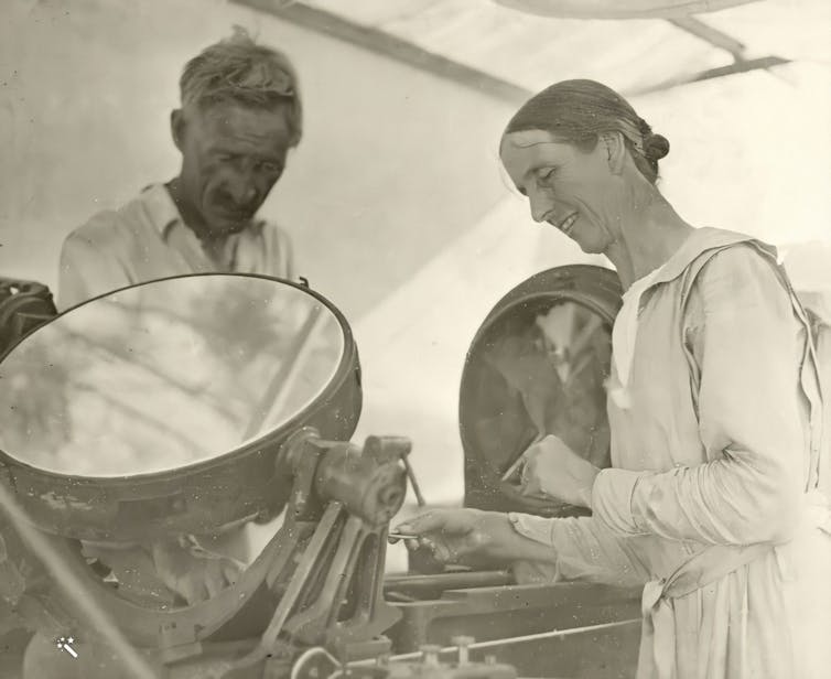 A man and a woman in tent adjusting a piece of equipment that has a circular mirror and pivots on one axis.