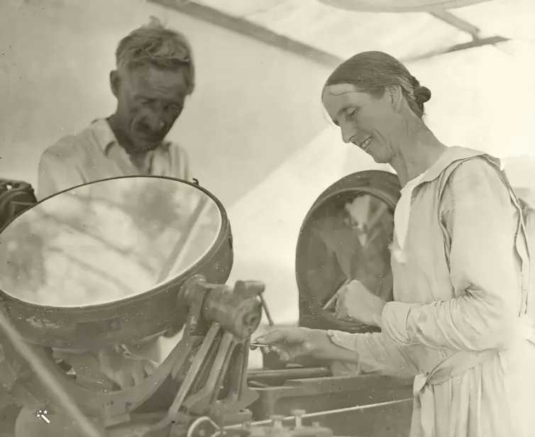 A man and a woman in tent adjusting a piece of equipment that has a circular mirror and pivots on one axis.