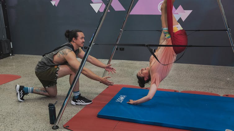 A woman in a gym, upside down in a harness.
