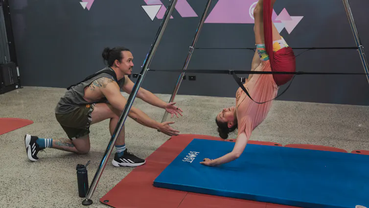 A woman in a gym, upside down in a harness.