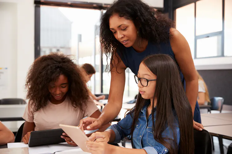 A teacher speaks to students working on laptops.