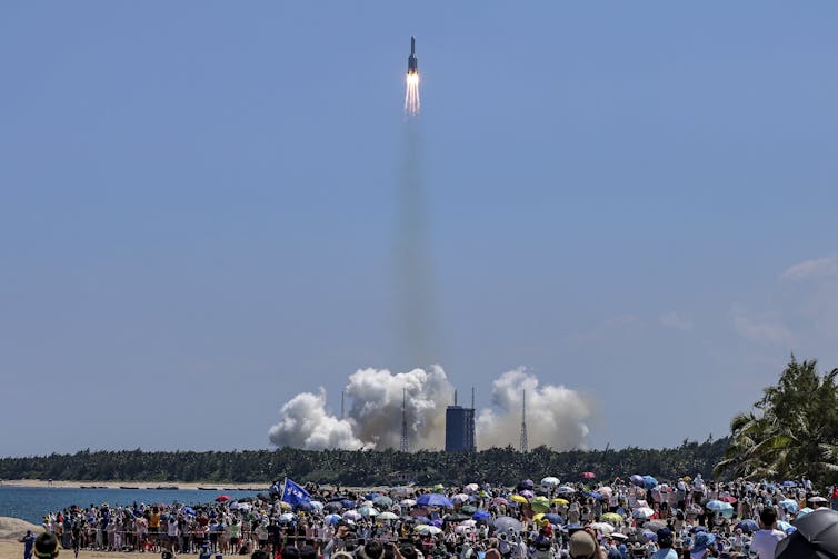 a photograph showing a rocket taking off in the distance while a crowd of people watch