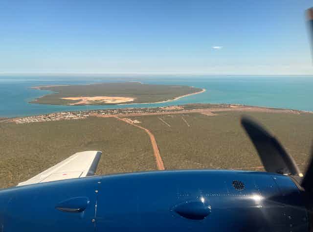 A photo taken from a plane shows a land and ocean below, with an island in the distance.