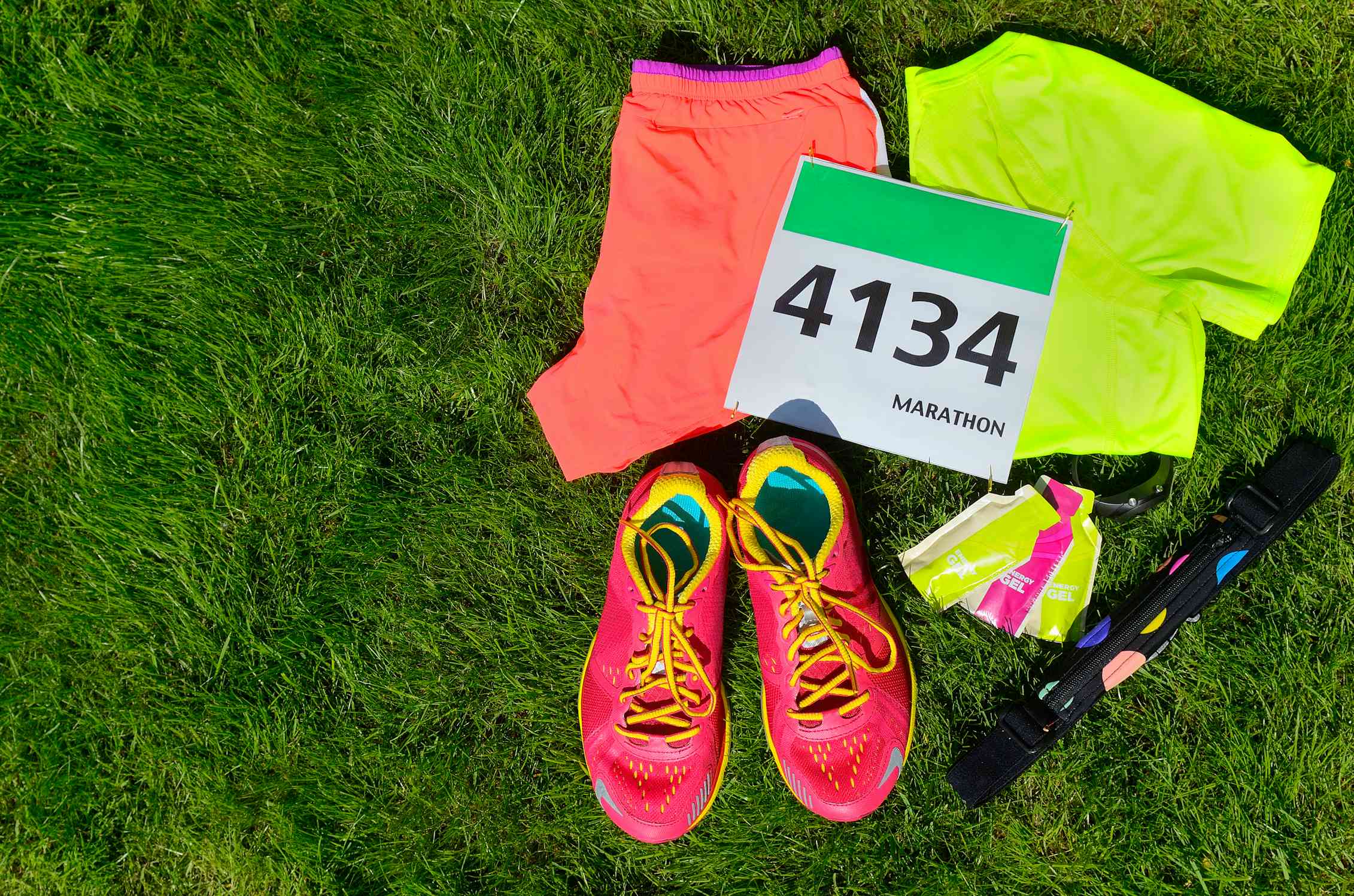 Runners kit including clothes, shoes, energy gels and competitor bib on grass