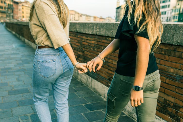 Two women hold hands while walking through a city.