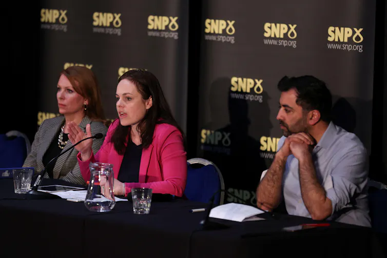 Ash Regan, Kate Forbes and Humza Yousaf sitting behind a long table at an event. Regan is speaking into a microphone.