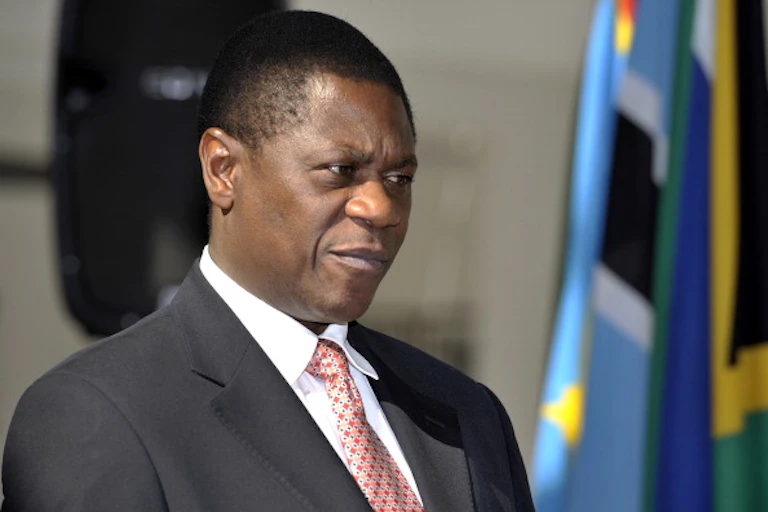 A man wearing a jacket and tie appears to be in a reflective mood next the flag of South Africa on his left.
