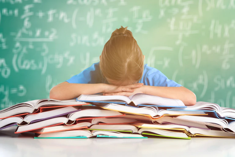 Une élève qui pose sa tête sur une pile de livres et de cahiers