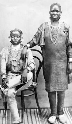 black and white photo of one Swahili woman seated on chair and another standing beside her