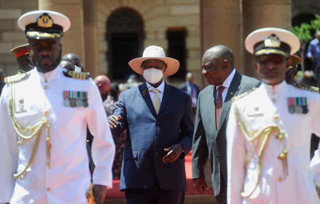 Ugandan president Yoweri Museveni with South African president Cyril Ramaphosa walking behind two men in military uniforms.