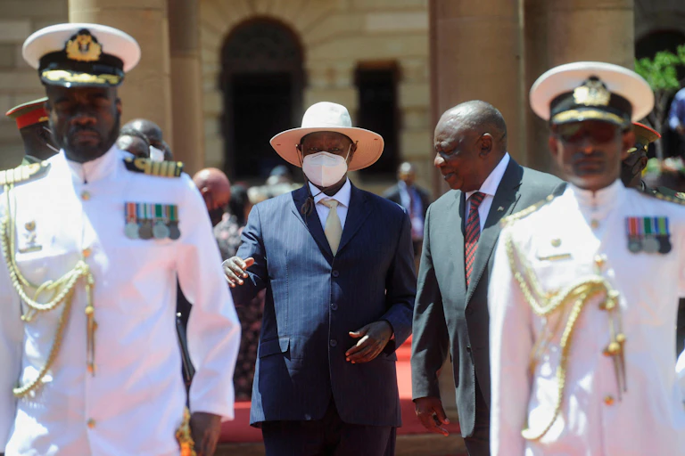 Ugandan president Yoweri Museveni with South African president Cyril Ramaphosa walking behind two men in military uniforms.