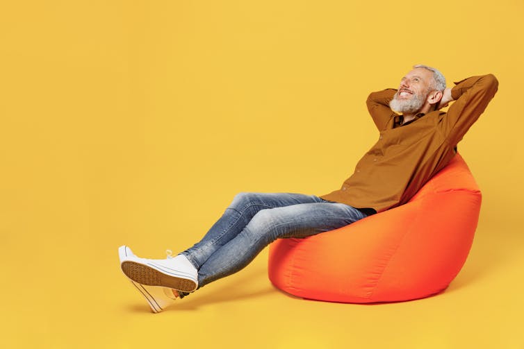 A man sitting on an orange beanbag doing the catapult body language position.