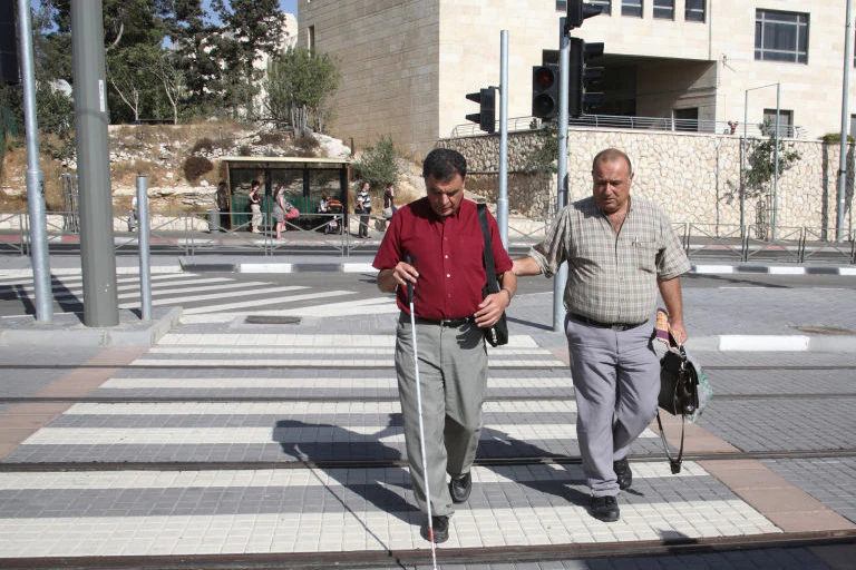 Man helps blind man with cane to cross the street.