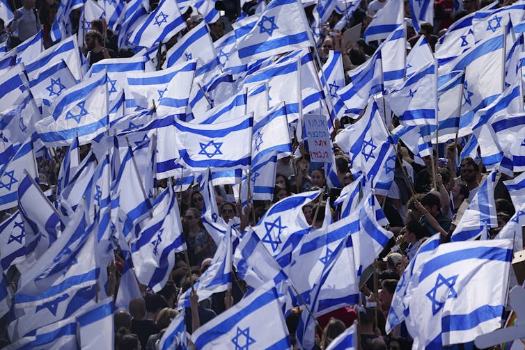 A sea of blue and white Israeli flags during a protest.
