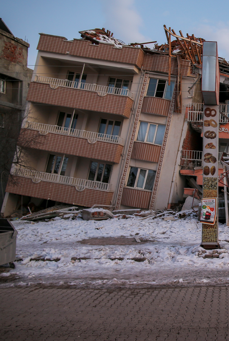 A partially collapsed tan building, leaning to the right side.