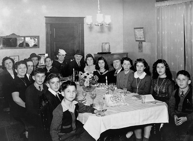 A black and white photo shows a large family gathered around a dining table