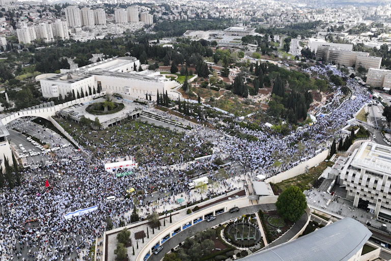 Thousands of people gathered on one side of a large complex of important-looking buildings.