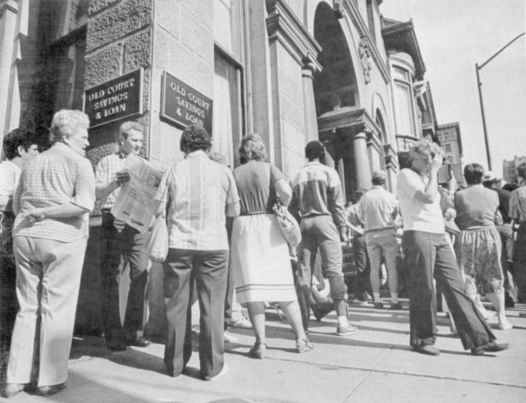 Black and white photo of people lined up outside a bank.