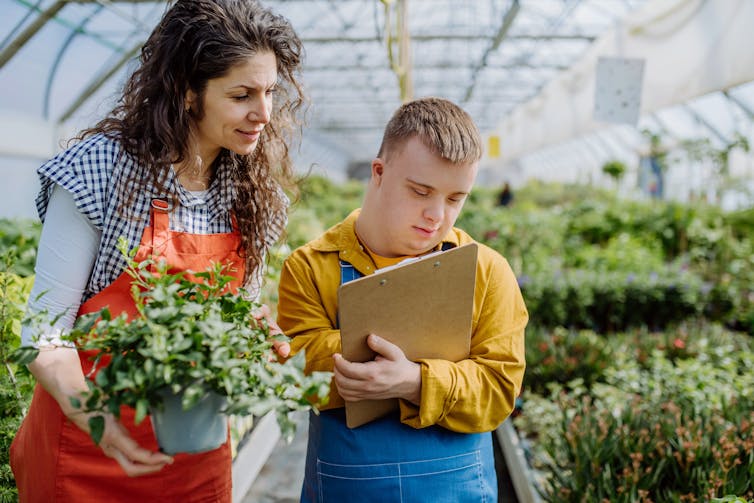 Woman and young man with disability working in large greenhouse
