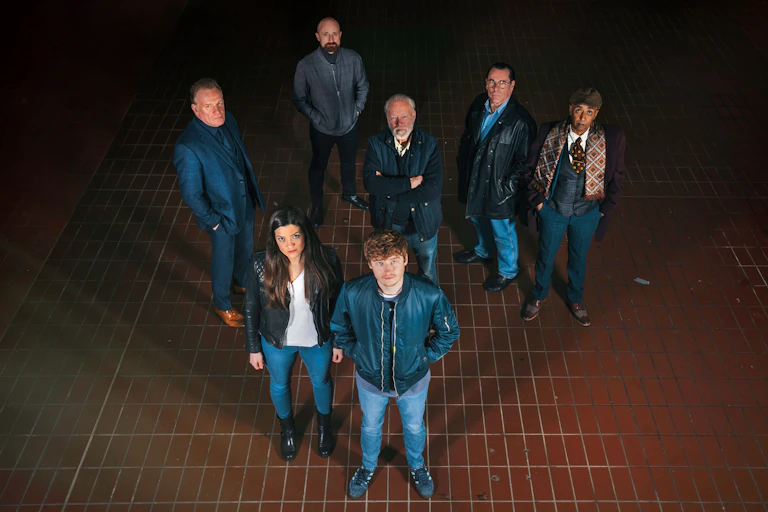A group of six men and one woman stare up at the camera.