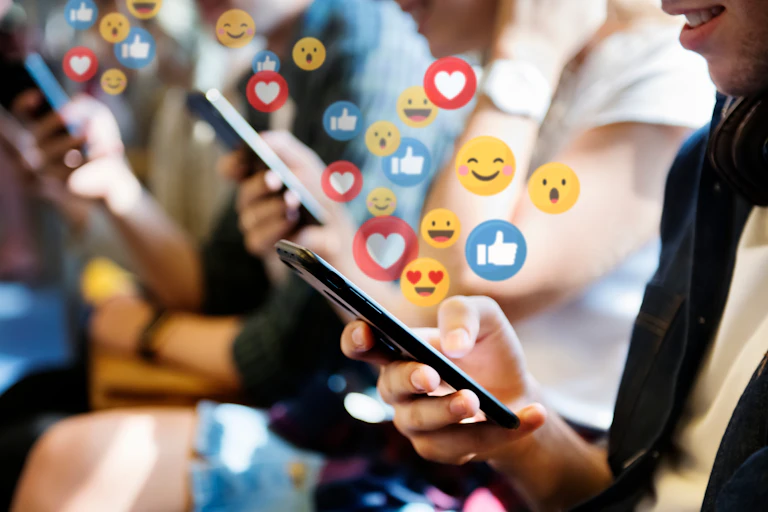 Young girls smiling as they look at their mobile phones, with 'thumbs up' 'smiley faces' and 'love' emojis rising from the screens