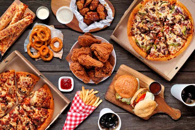 Fast food (pizza, burders, fried chicken, fried onion rings) displayed on a table