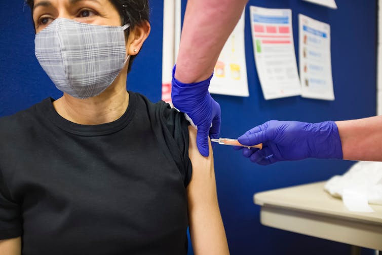 A woman wearing a face mask receives a vaccine.