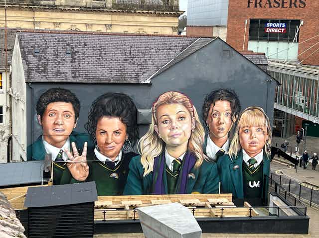 A two-story mural of teenagers in green uniforms covers the side of a building.
