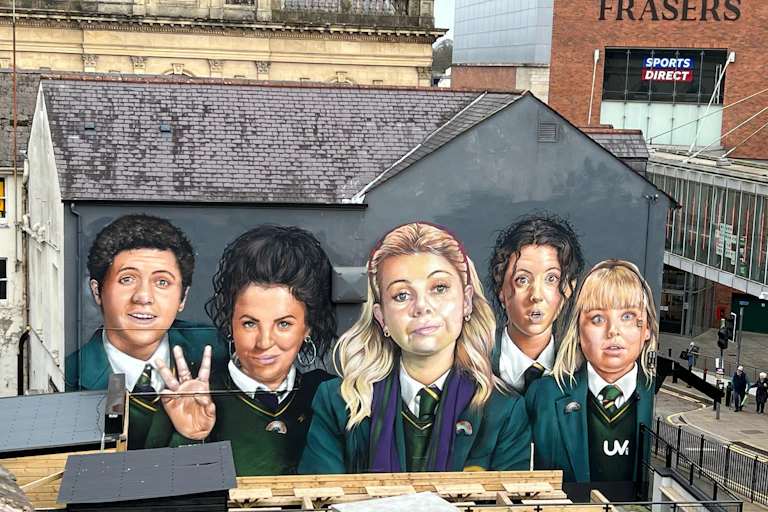 A two-story mural of teenagers in green uniforms covers the side of a building.