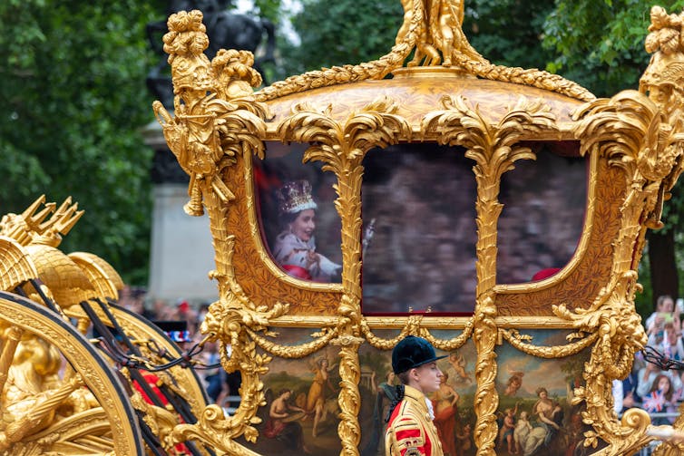 The ornate, golden coronation carriage with a hologram of a young Queen Elizabeth appearing on the window.