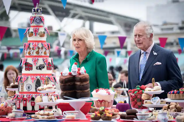 Charles and Camilla stand at a table filled with strawberries, baked treats, and a seven-tier cake decorated with symbols of London and the queen.