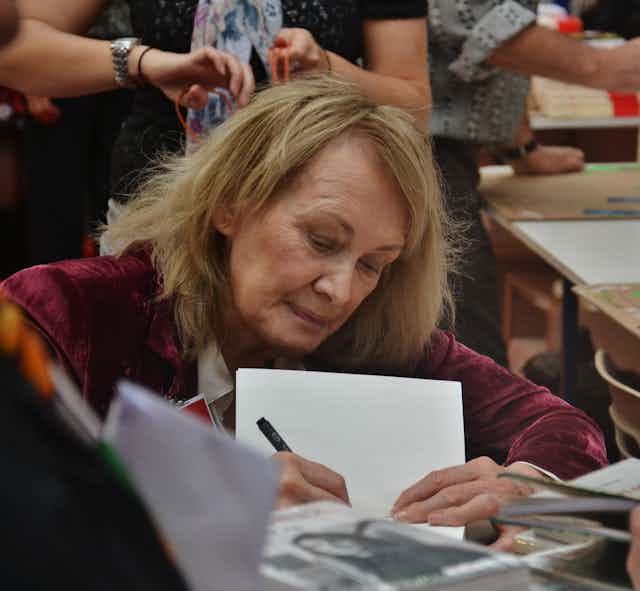 Una mujer firma libros en una feria del libro.