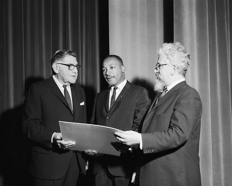 Two men in suits stand on either side of Martin Luther King, Jr. as they hand him an award.