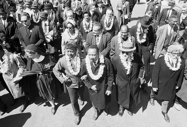 A black and white photo shows rows of marchers wearing leis.