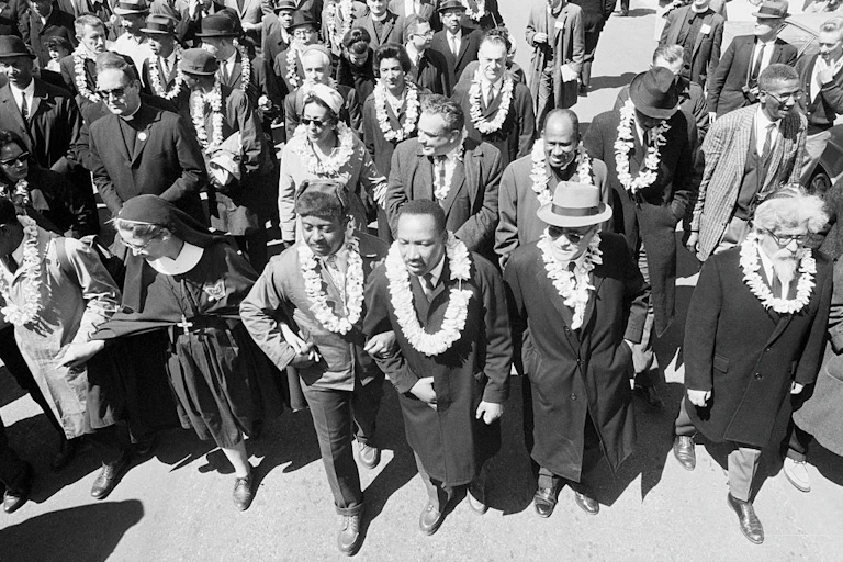 A black and white photo shows rows of marchers wearing leis.