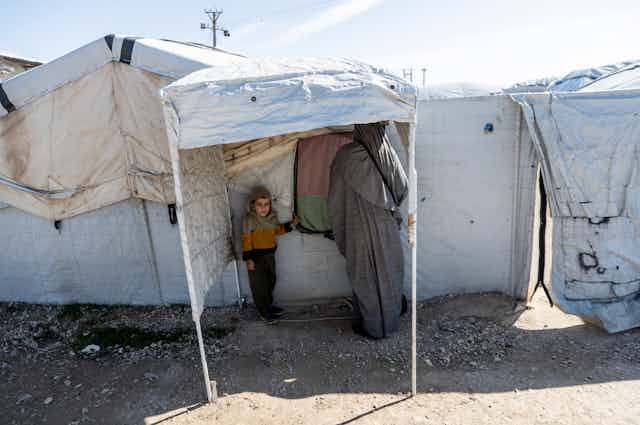 A woman and child stand under a canopy in detention camp.