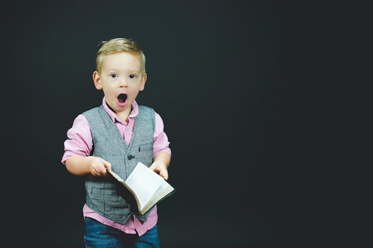 Un niño sujeta un libro y abre la boca, sorprendido.