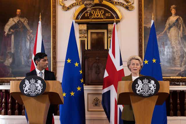 Two people stand behind matching lecterns with flags of the European Union and the United Kingdom behind them.