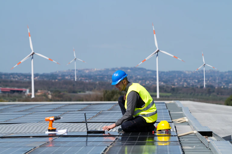 Un technicien contrôle des panneaux solaires avec des éoliennes dans le fond de l'image
