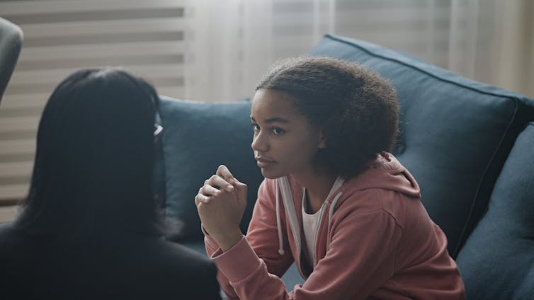 A young girl sits on a couch talking with a woman.
