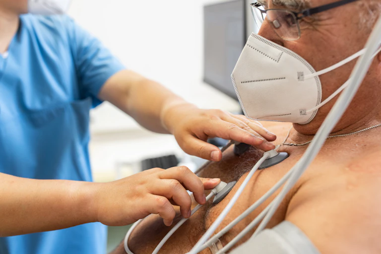 Close-up of a doctor attaching electrodes on patient's chest to monitor electrocardiogram in clinic.