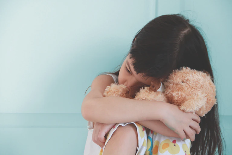 young girl cuddles toy and hides face