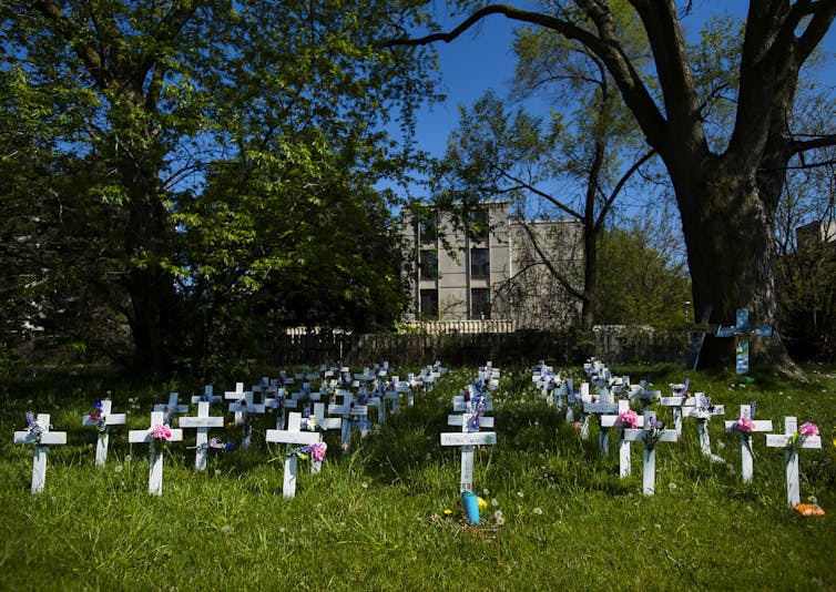 Rows of small white crosses on a lawn with a building in the background
