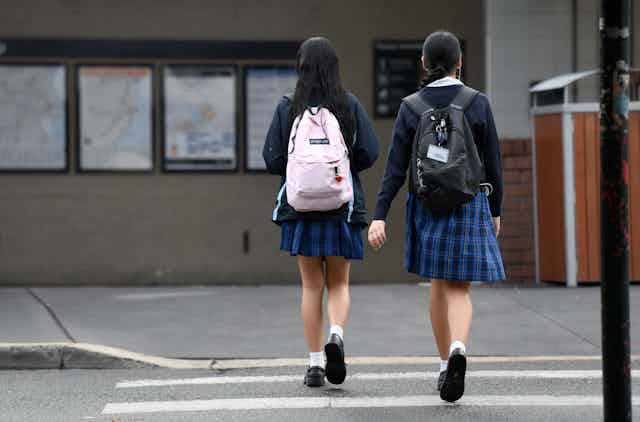 Two students in school uniform cross the road.