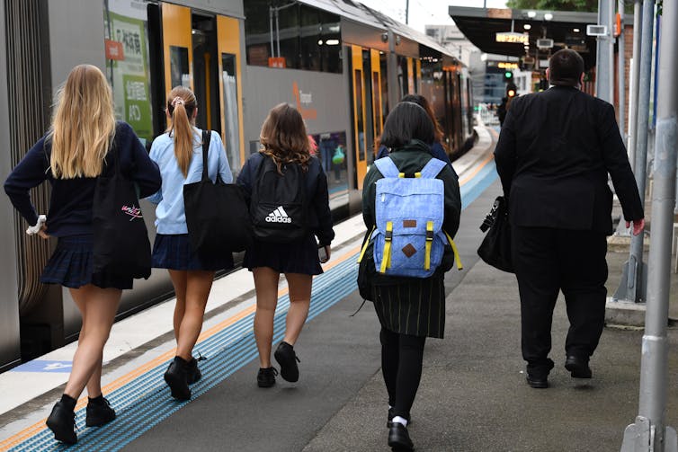 School students walk along a train platform.