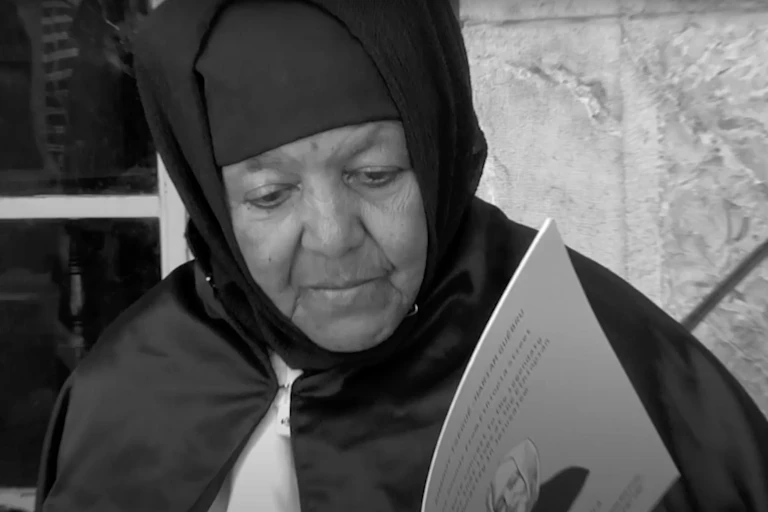 A black and white image of an elderly woman in nun's habit reading from a book of sheet music.
