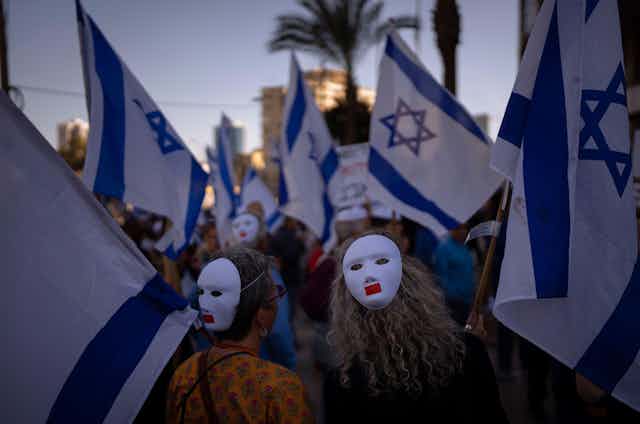 Masked anti-government protesters wearing masks and carrying Israeli flags.